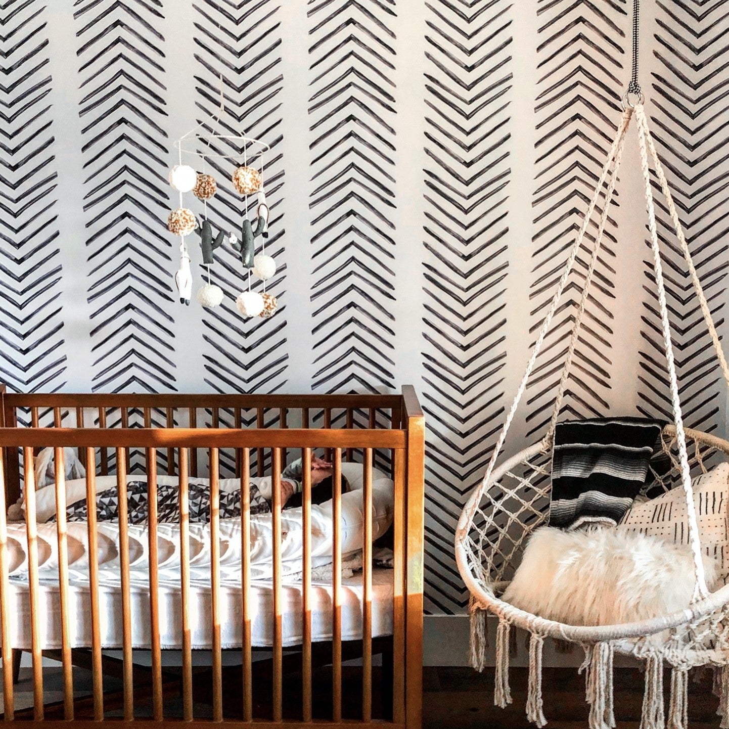 "Ar-row Wallpaper by Wall Blush in a stylish nursery room, featuring crib and hanging chair with wallpaper as focus."