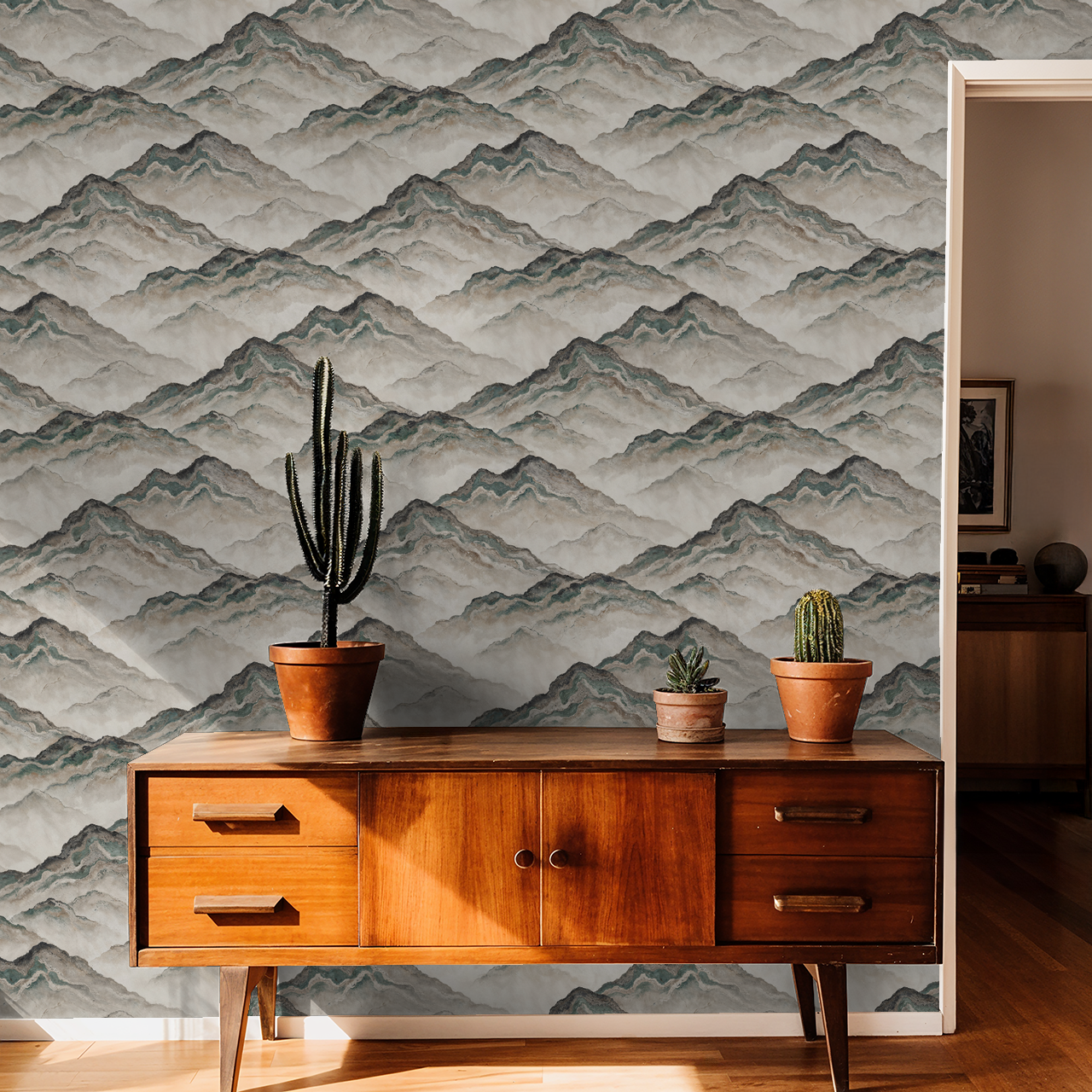 Mountain wave wallpaper in earthy tones with wooden sideboard and cacti decor.