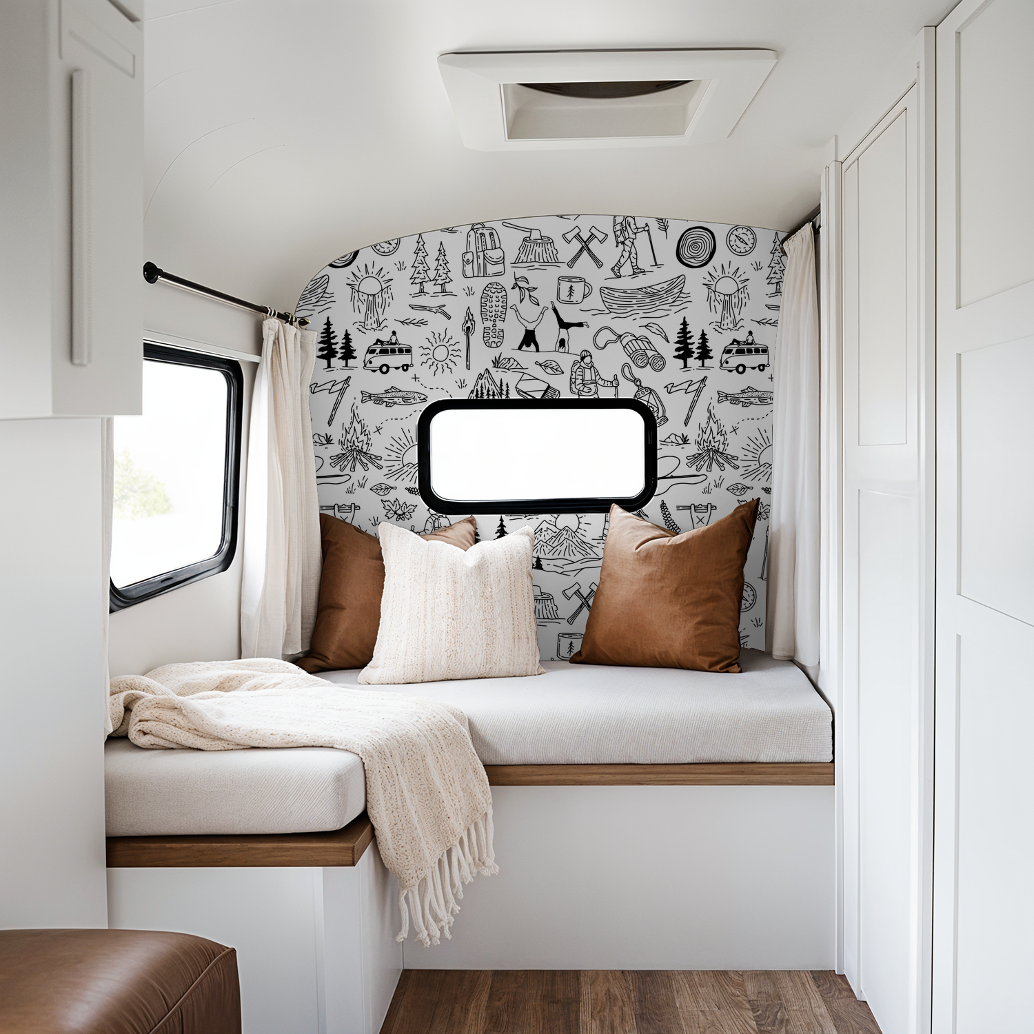 Black and white adventure-themed wallpaper in cozy RV interior with pillows.