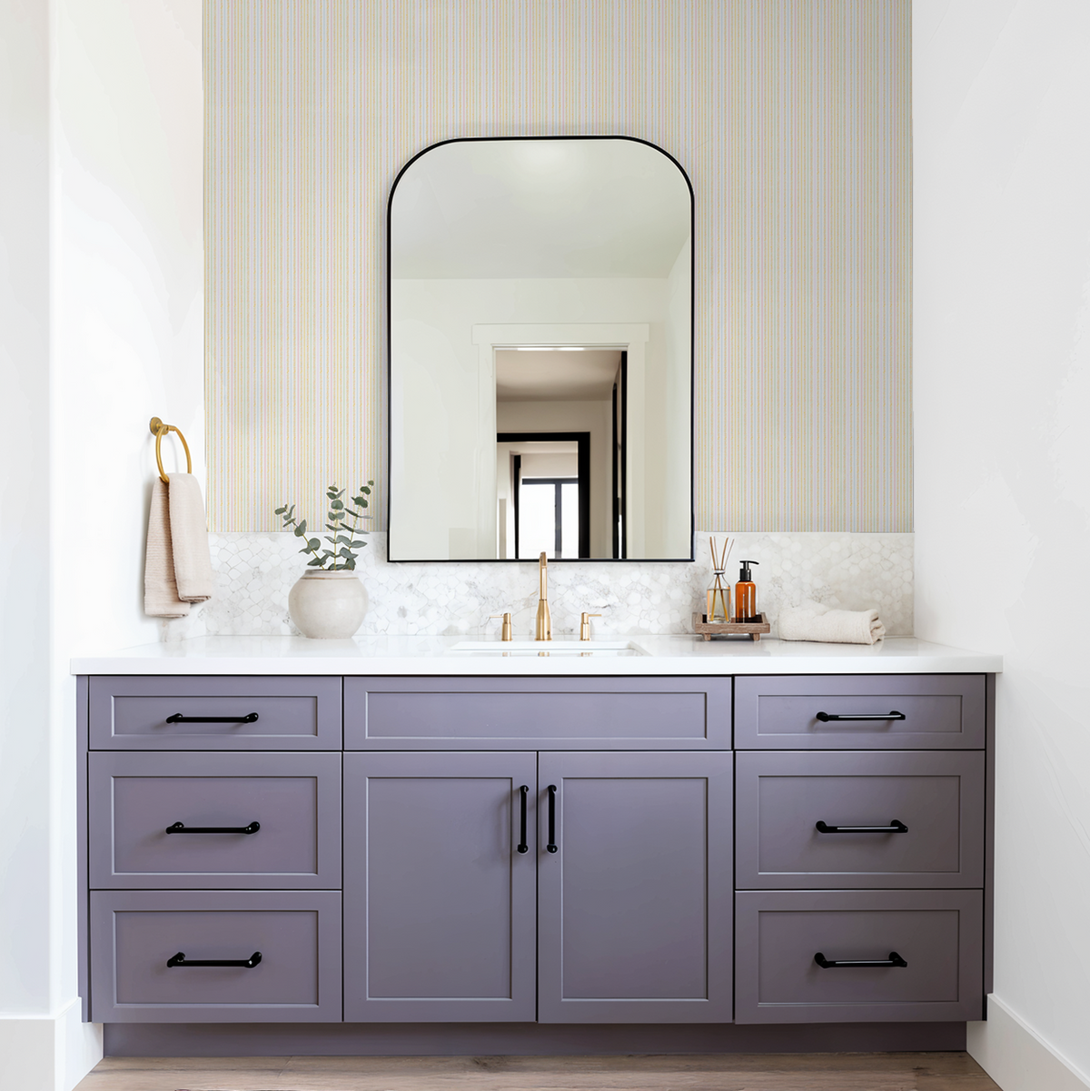 Pastel striped wallpaper in bathroom with purple vanity and gold fixtures.