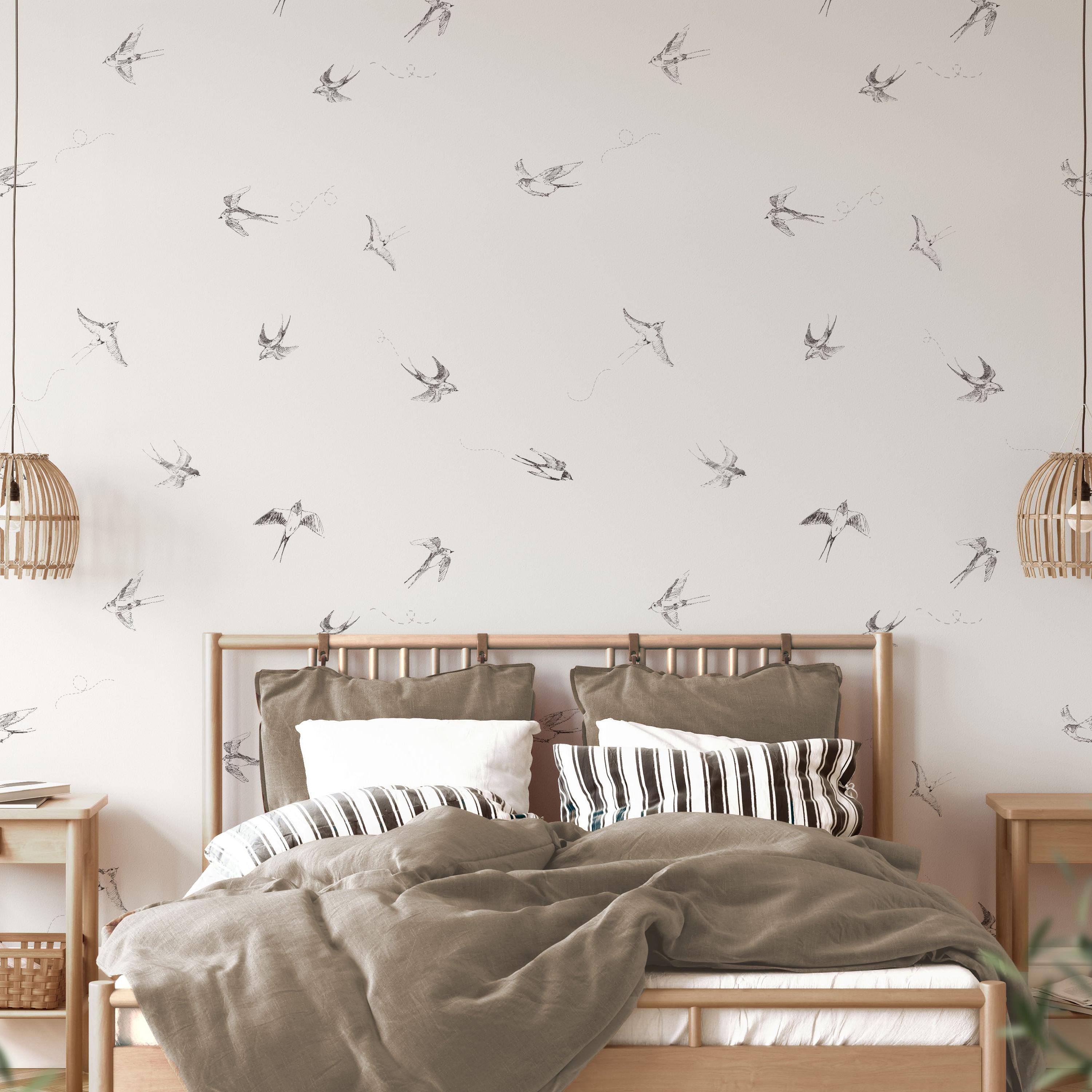 "Wall Blush's 'Of a Feather (White)' wallpaper featured in cozy bedroom setting, showcasing elegant bird design."