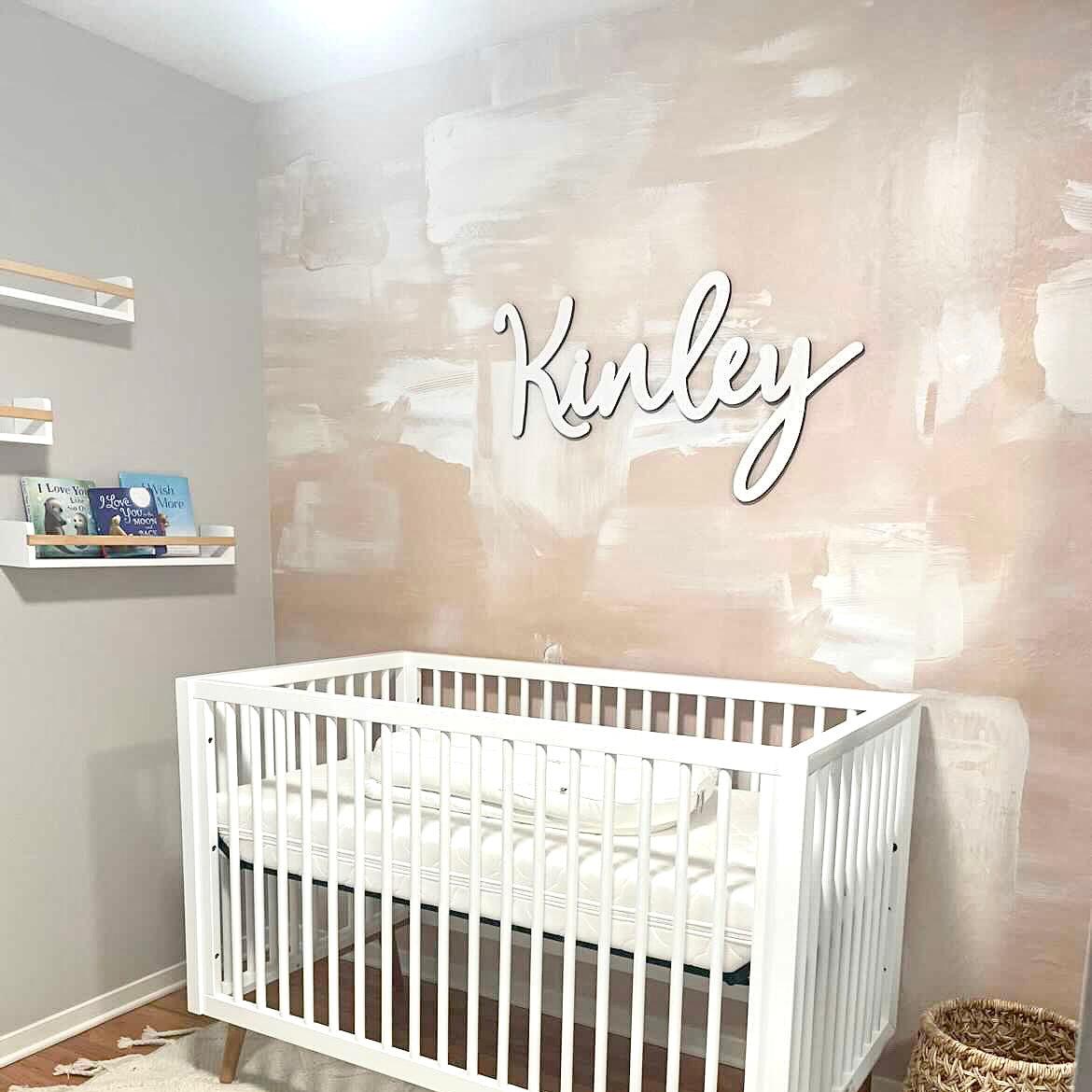Glide Wallpaper from The Minty Line accentuates the nursery's wall behind white crib and decorative name sign.