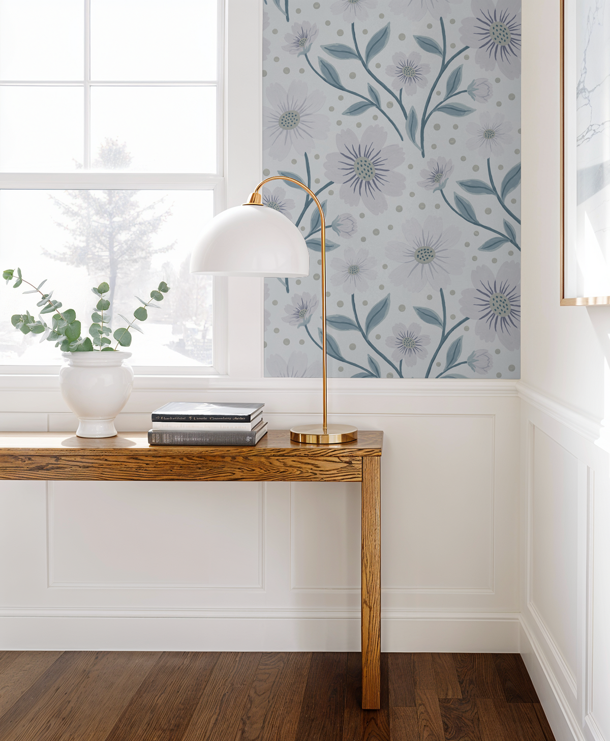 Floral wallpaper with lilac blooms in a bright room with wooden table and lamp.