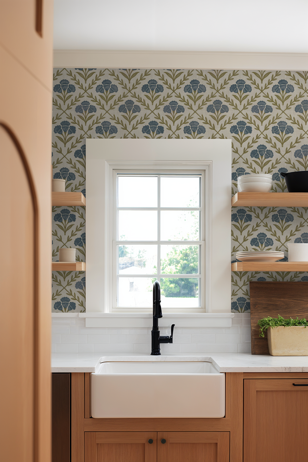Kitchen with blue floral wallpaper, wooden cabinets, and white sink