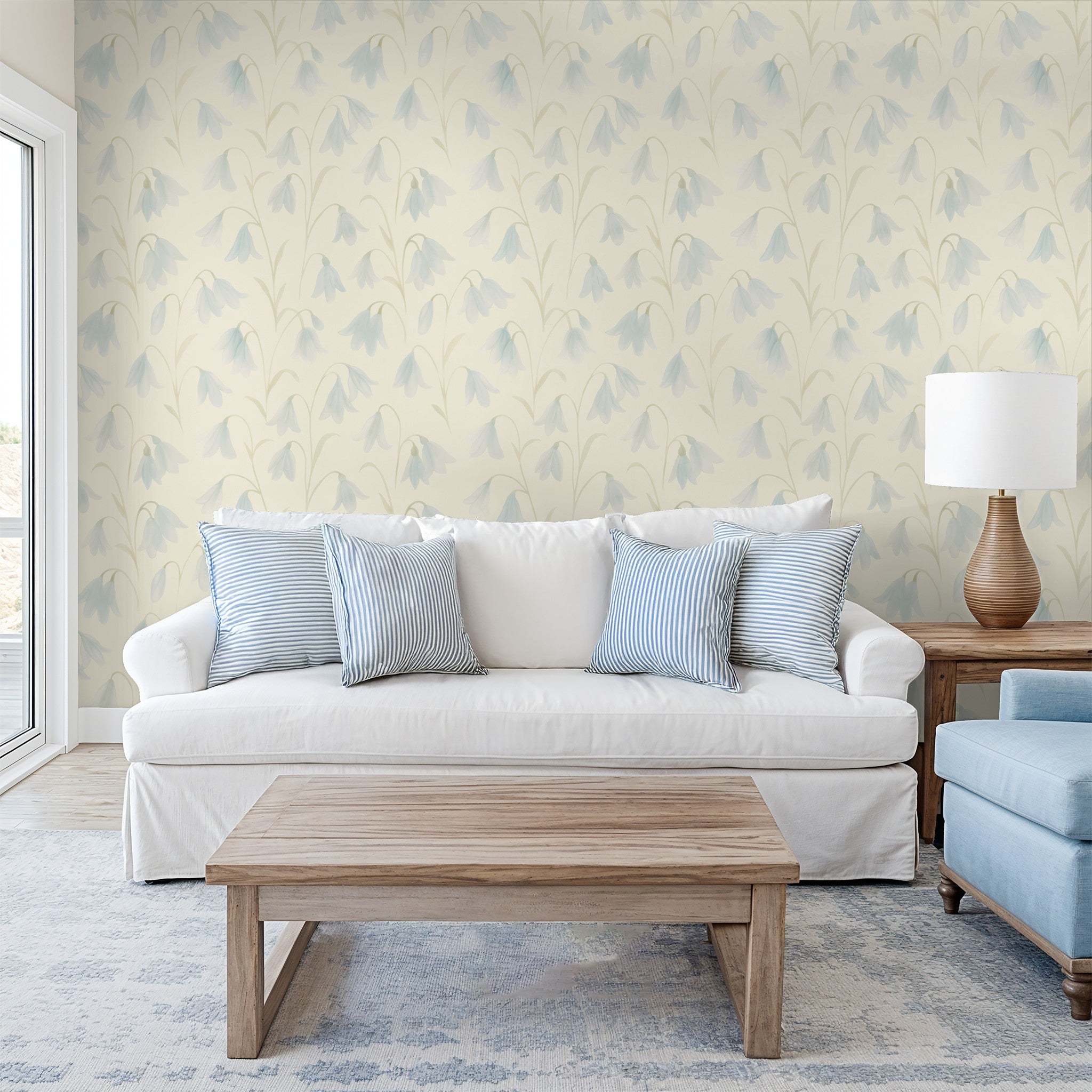 English Bluebells wallpaper in sunlit room with cream and blue floral design, white sofa, and light wood furniture.