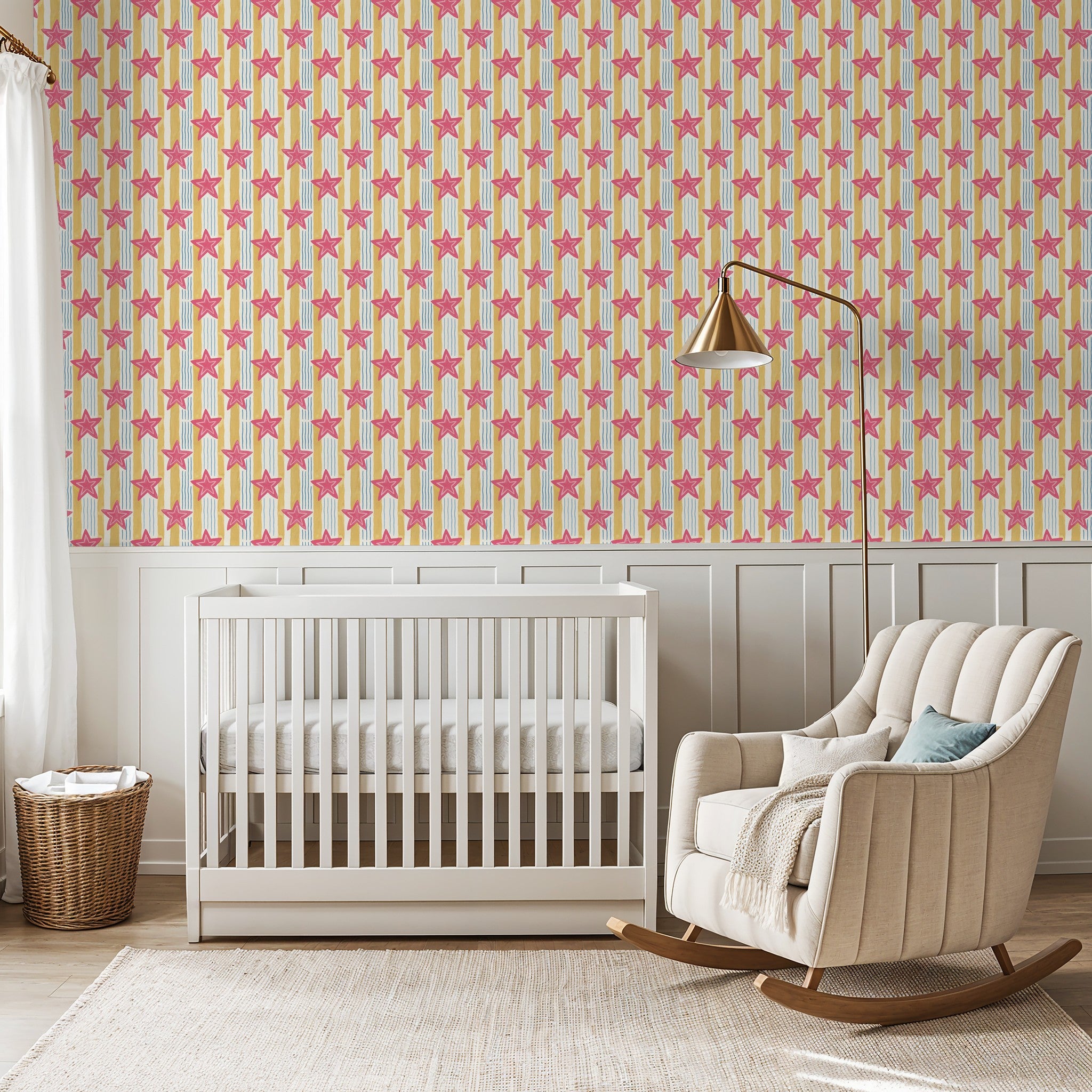 Pink star wallpaper with yellow and blue stripes in a nursery with crib and rocking chair.